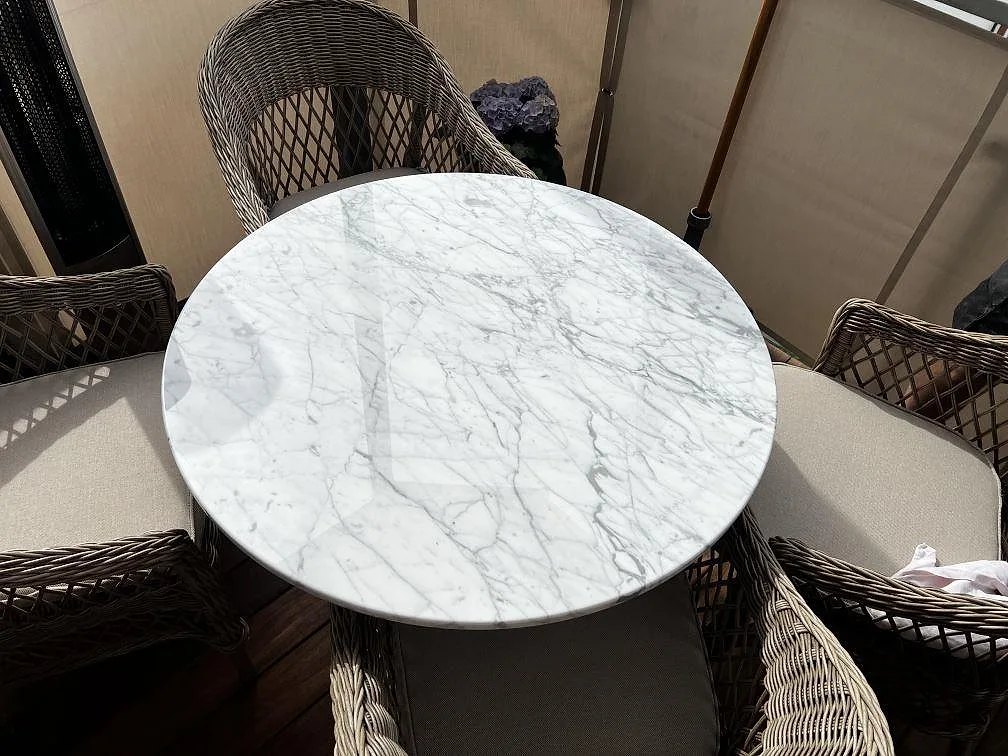 Rund bordsskiva i polerad Carrara C marmor med grå ådring på ett matbord i Helsingborg.