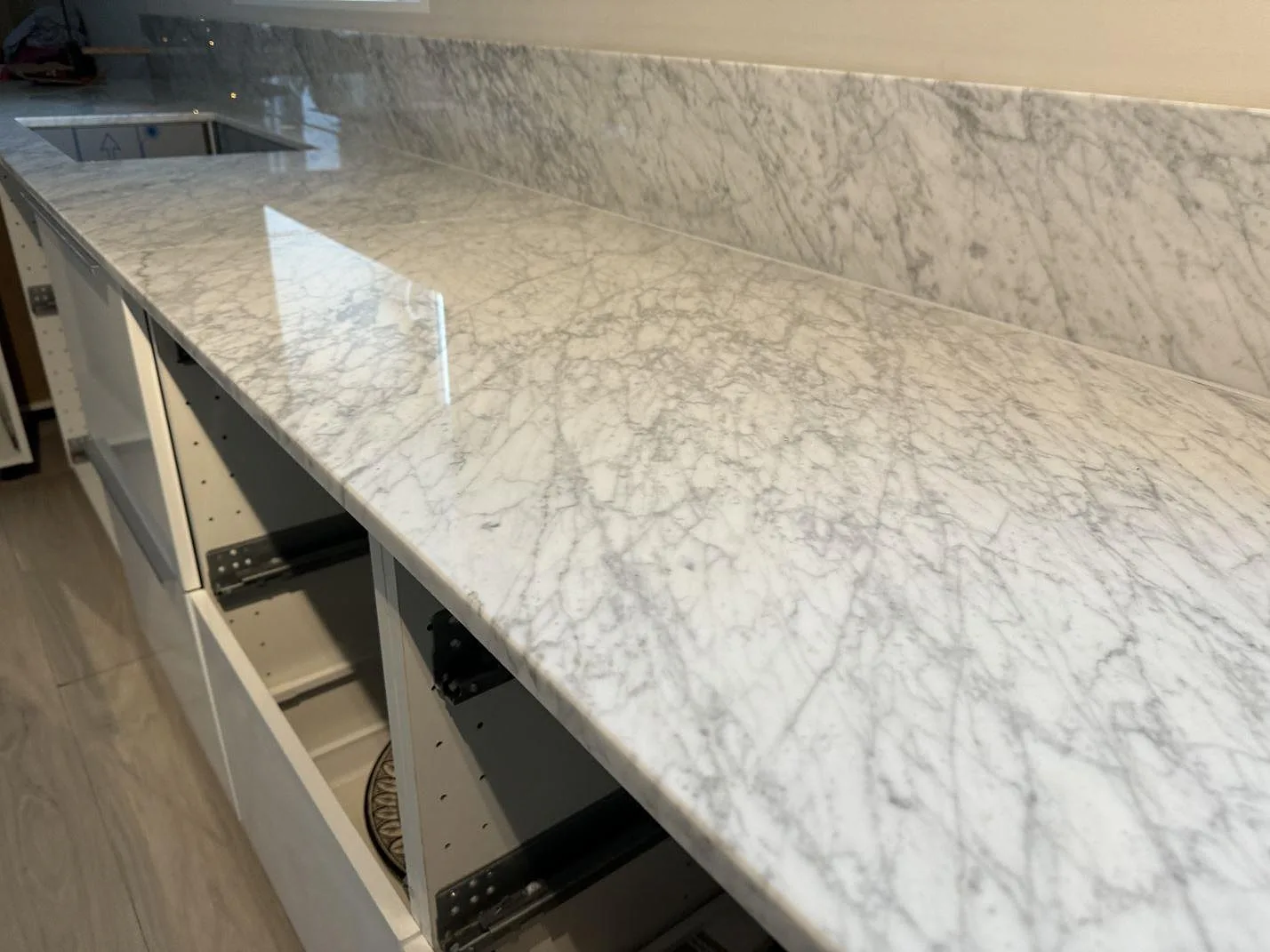 Närbild på underlimmad rostfri diskho i polerad Carrara C-marmor med blandarhål och skyddsinsats i Höganäs.