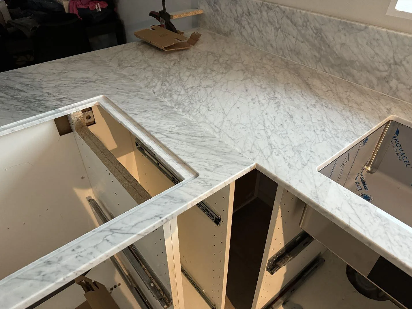 Köksbänkskiva i polerad Carrara C-marmor med uppvikt stänkkant under fönster och vita köksstommar i Höganäs.