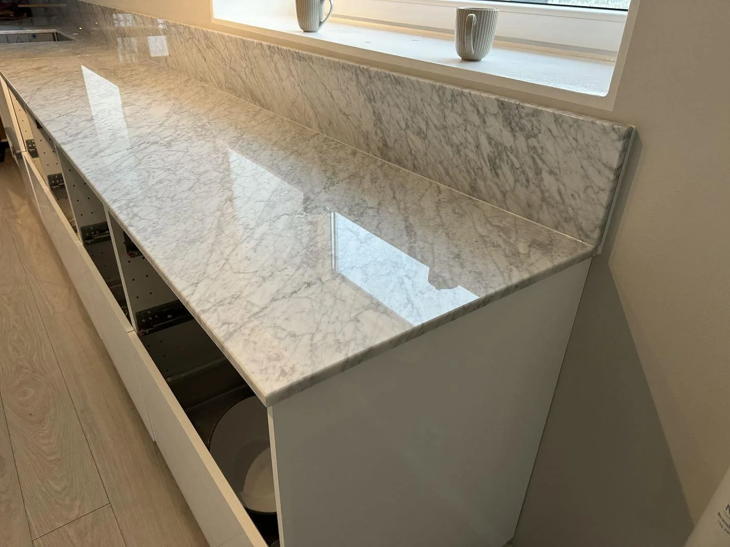 Detalj av polerad Carrara C-marmor med grå ådring och uppvikt stänkkant längs köksväggen i Höganäs.