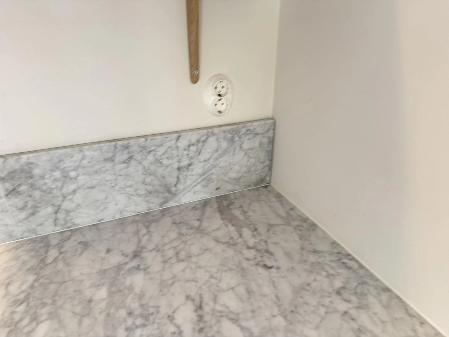 Detalj av matt Carrara C marmor på bänkskiva och stänkkant vid ett ljust kökshörn i Höllviken.