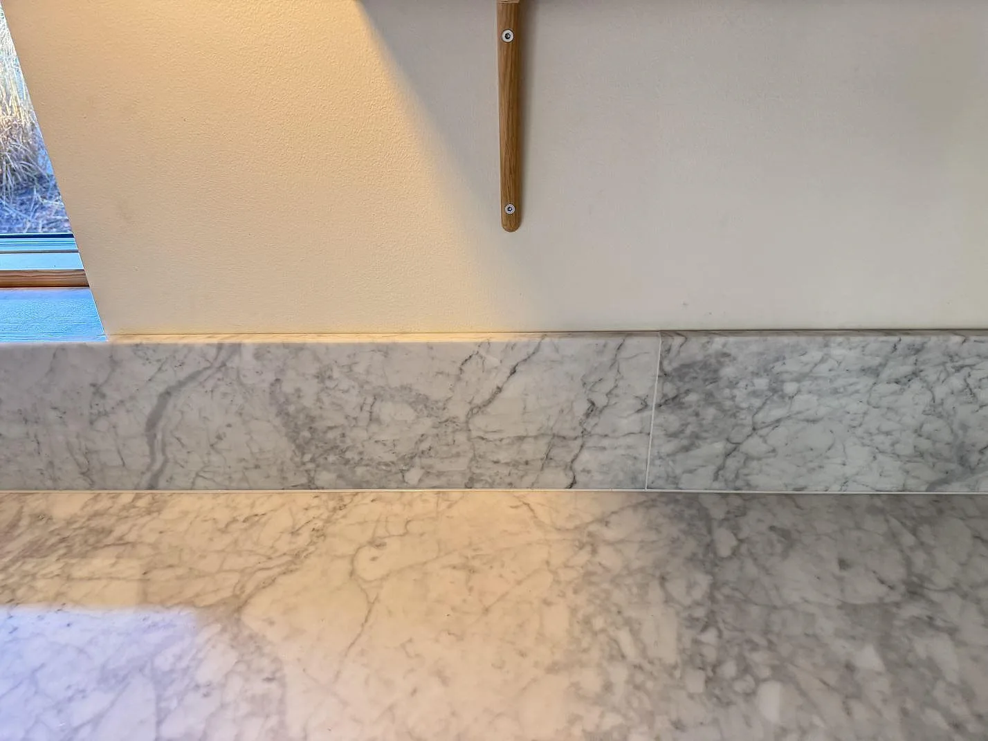 Rak köksvägg med matt Carrara C marmor som bänkskiva och stänkkant under väggfästen i Höllviken.