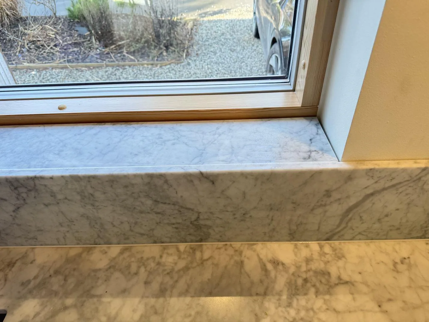 Närbild på fönsterbänk och stänkkant i matt Carrara C marmor ovanför köksbänkskivan i Höllviken.