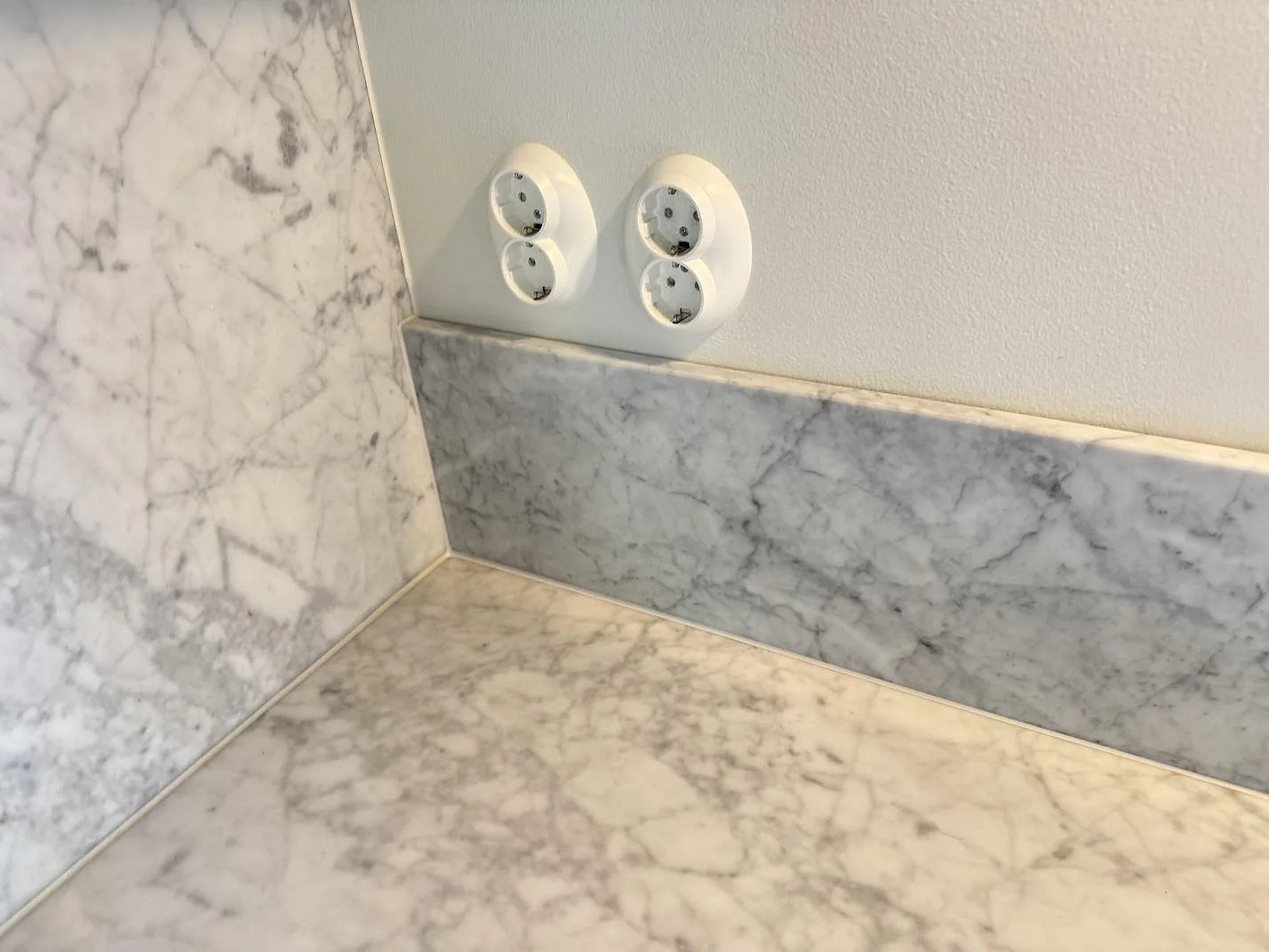 Hörn med köksbänkskiva, väggskiva och uppvikt stänkkant i matt Carrara C marmor i Höllviken.