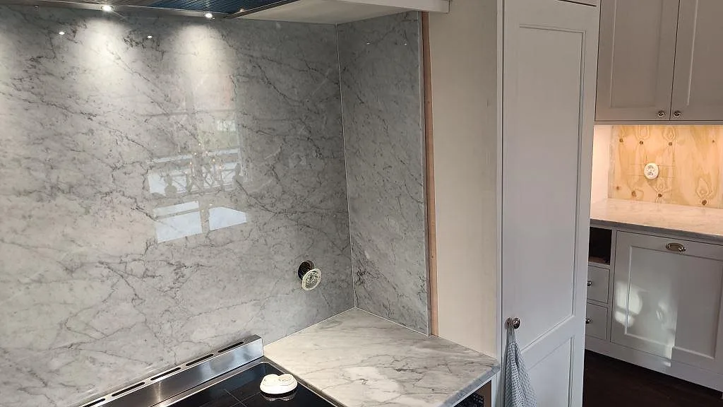 Polerad Carrara C marmor som stänkskydd bakom spisen, med grå ådring och ljus köksinredning i Hovås.