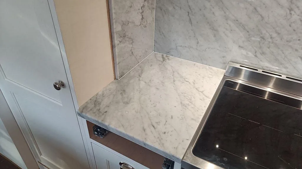 Hörnvy av Carrara C bänkskiva och polerat marmorstänkskydd vid spisen i ett kök i Hovås.