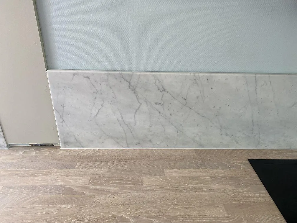 Väggbeklädnad i matt Carrara C-marmor med tydlig grå ådring monterad bakom köksbänken i Jægerspris.