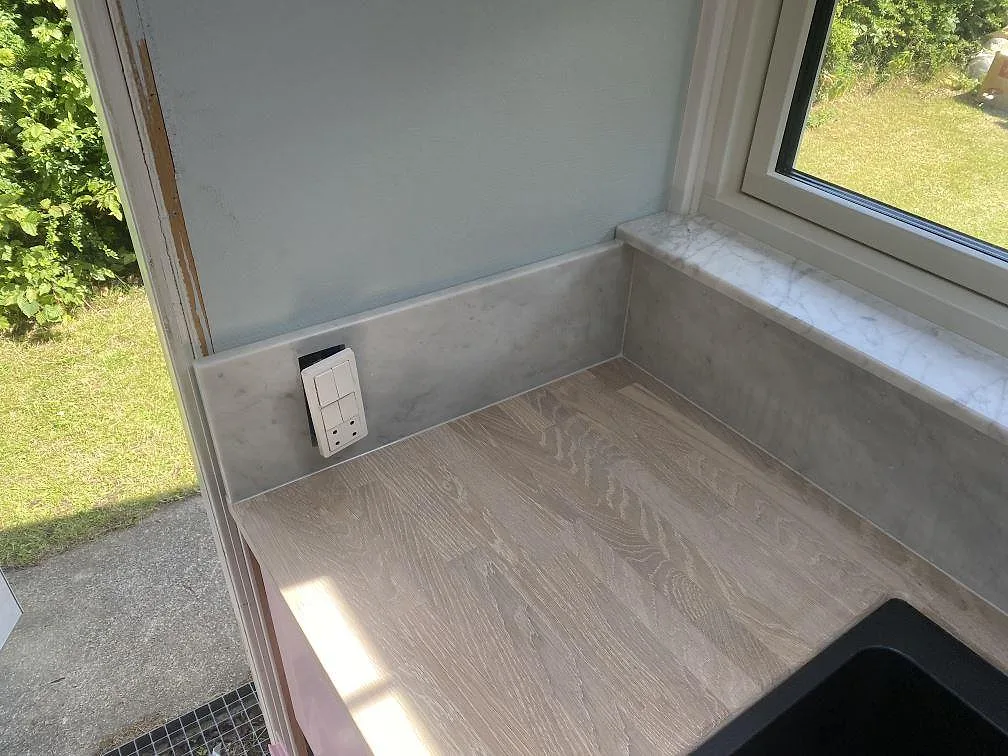 Hörn med fönsterbänk i Carrara C-marmor och eluttag ovanför arbetsytan i ett kök i Jægerspris.