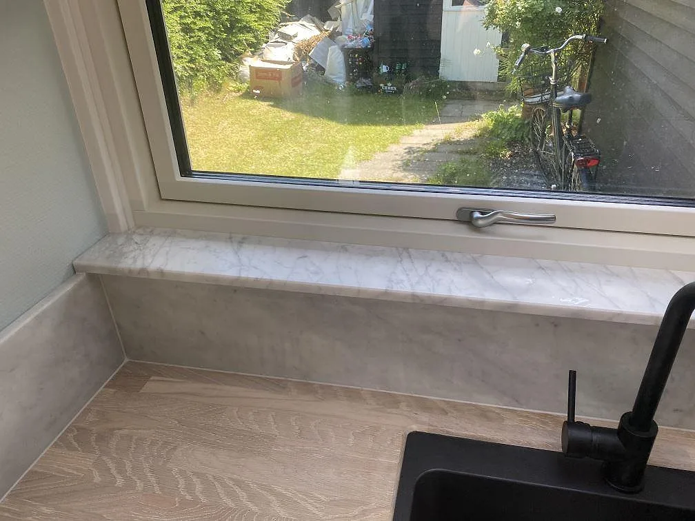 Fönsterbänk i matt Carrara C-marmor vid köksfönster med svart köksblandare och svart kompositdiskho i Jægerspris.