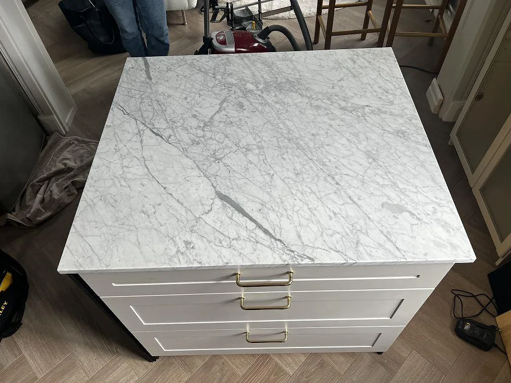 Marmorbänkskiva i matt Carrara C, 20 mm, monterad på vit köksinredning med mässingshandtag i Jönköping.