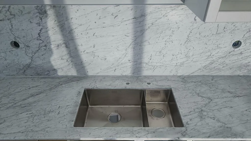 Matt köksbänkskiva i Carrara C marmor med rostfri diskho och matchande stänkskiva i ett kök i Klagstorp.