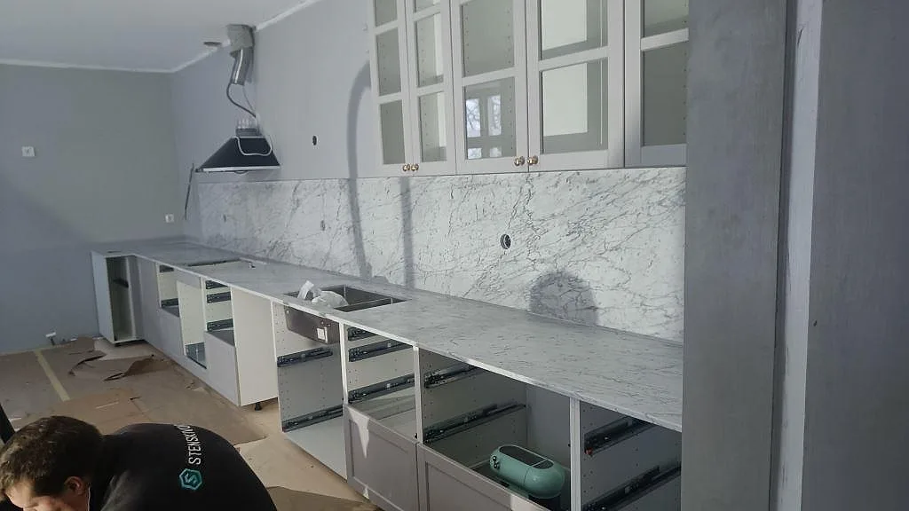 Köksbänkskiva i Carrara C-marmor, matt, längs en hel köksvägg med matchande heltäckande stänkvägg under montering i ett kök i Klagstorp.