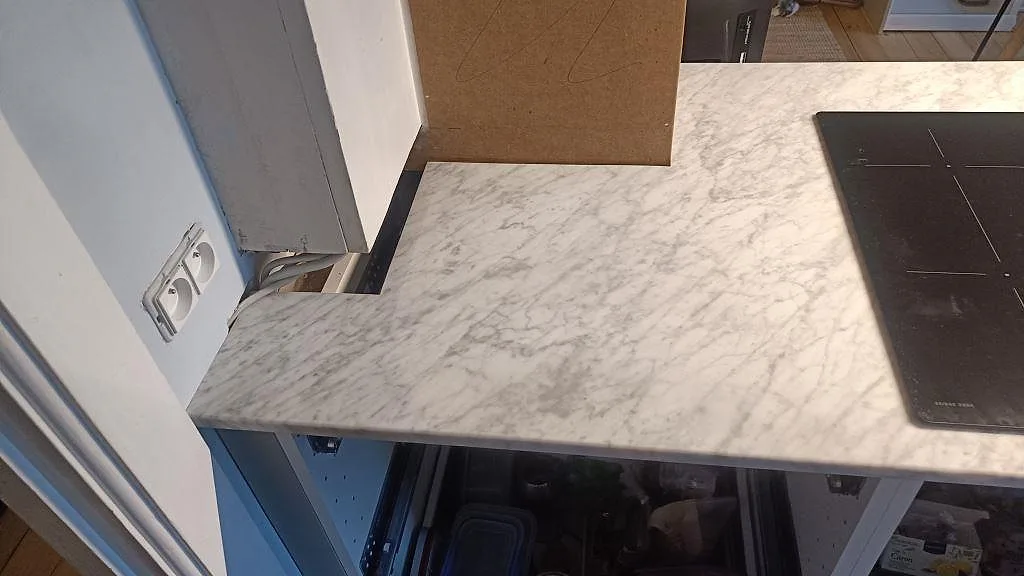 Halvö i polerad Carrara C marmor intill svart induktionshäll och öppna köksstommar i København Ø.