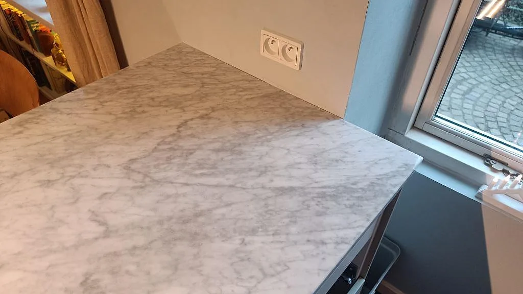 Avslutande bänkyta i polerad Carrara C marmor vid fönster och vägguttag i ett kök i København Ø.