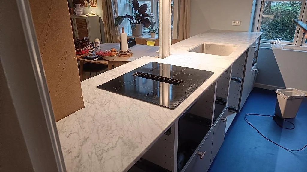 Köksbänkskiva i polerad Carrara C marmor med L-form, halvö, svart induktionshäll och underlimmad rostfri diskho i København Ø.
