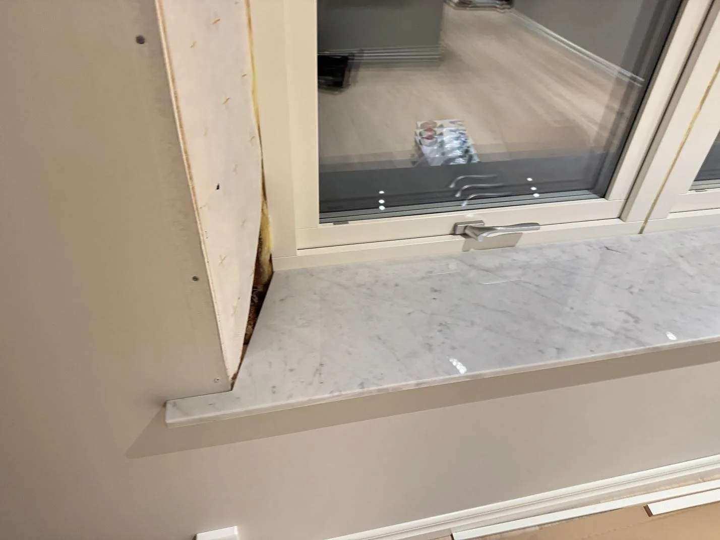Närbild av polerad Carrara C fönsterbänk i marmor under fönsterkarmen i Kristianstad, med grå ådring och blank yta.