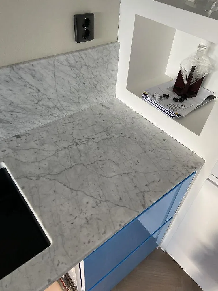 Köksbänkskiva i Carrara C marmor som möter köksö i samma marmor i ett ljust kök i Landskrona.