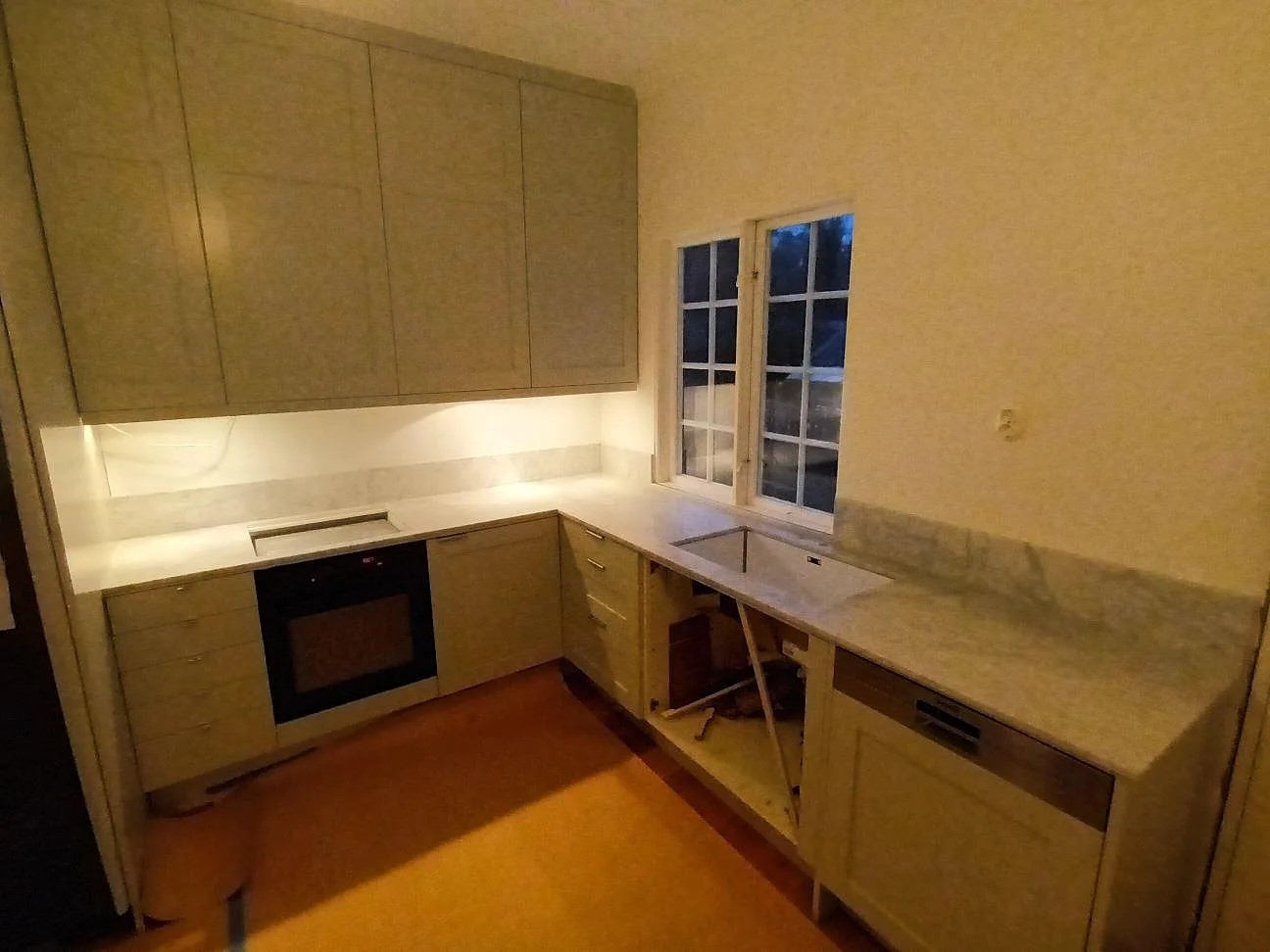 Köksbänkskiva i vit Carrara C marmor, matt, med underlimmad diskho och uppvikt stänkkant i ett L-format kök under montering i Lidingö.