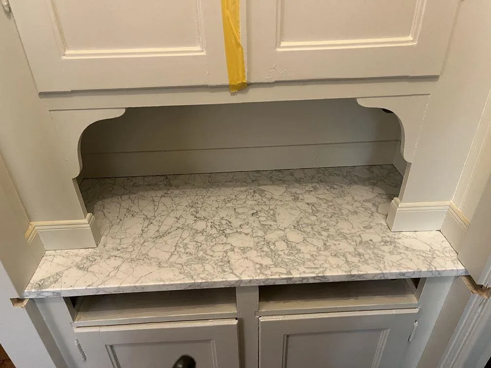 Bänkskiva i matt Carrara C marmor under fönster med profilerade luckor i ett kök i Lidingö.