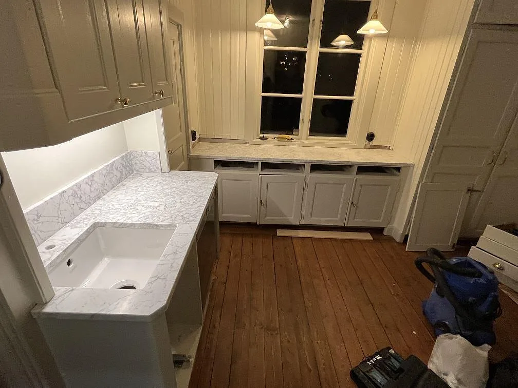 Köksbänkskiva i matt Carrara C marmor med underlimmad ho, uppvikt stänkkant och bänkyta under fönster i Lidingö.