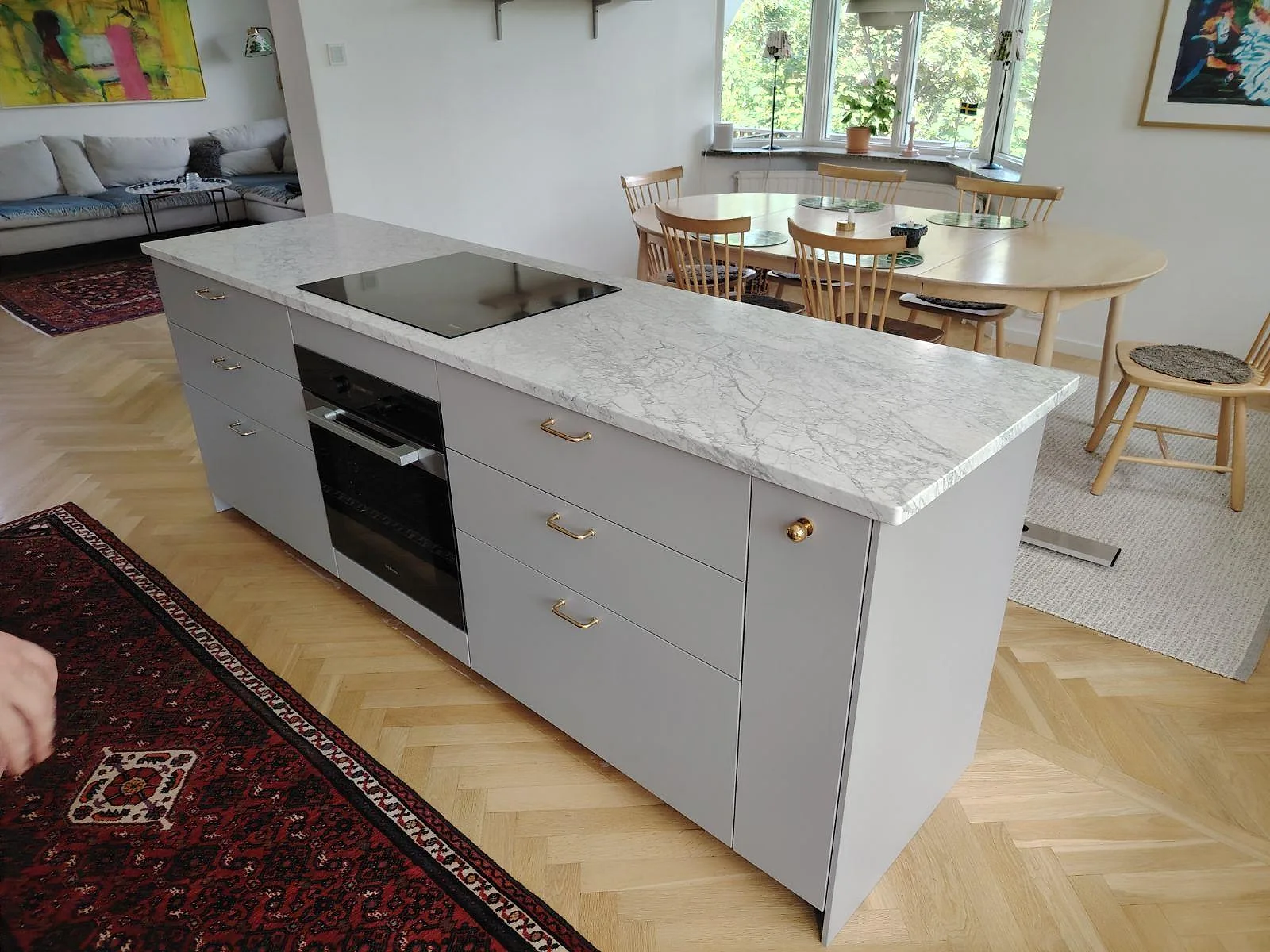 Köksbänkskiva i matt Carrara C marmor på en fristående köksö med svart induktionshäll och integrerad ugn i Lidingö.