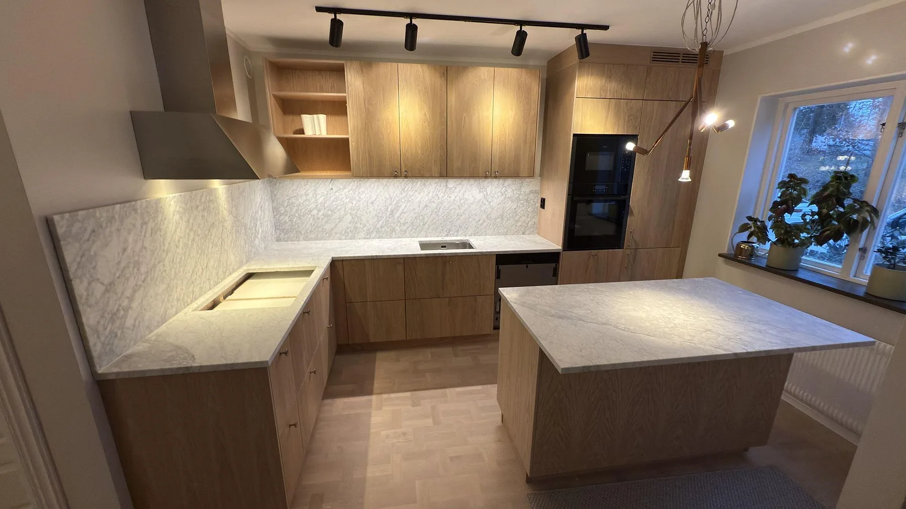 Köksbänkskiva i vit Carrara C-marmor, matt, U-formad med heltäckande stänkskydd och fristående köksö i ett kök på Lidingö.