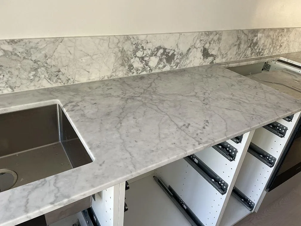 Närbild på matt Carrara C-marmor med underlimmad rostfri diskho, hälluttag och lågt stänkskydd i Lindome.