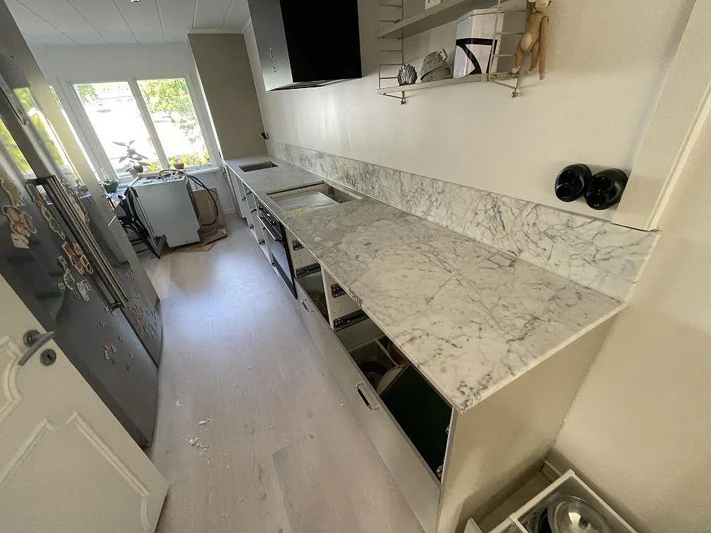 Köksbänkskiva i matt Carrara C-marmor med matchande stänkskydd i ett smalt kök i Lindome under montering.