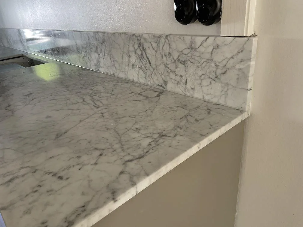 Sidoavslut på matt Carrara C-marmorbänkskiva med lågt stänkskydd och vita köksstommar i Lindome.