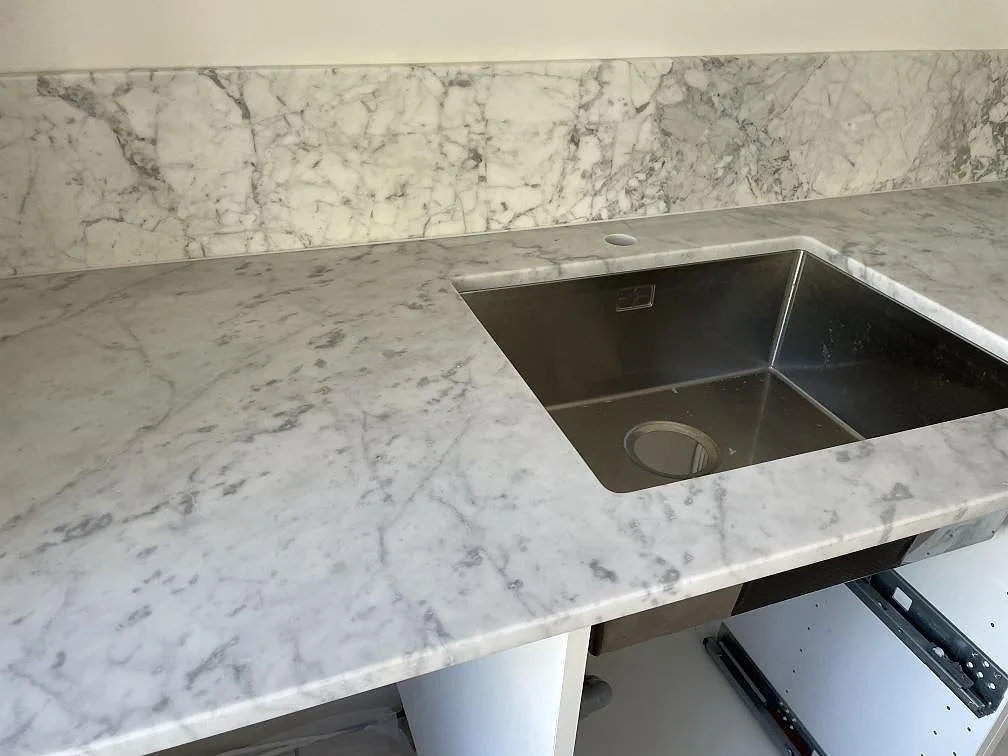 Rostfri underlimmad diskho infälld under en matt Carrara C-marmorbänkskiva med grå ådring i Lindome.
