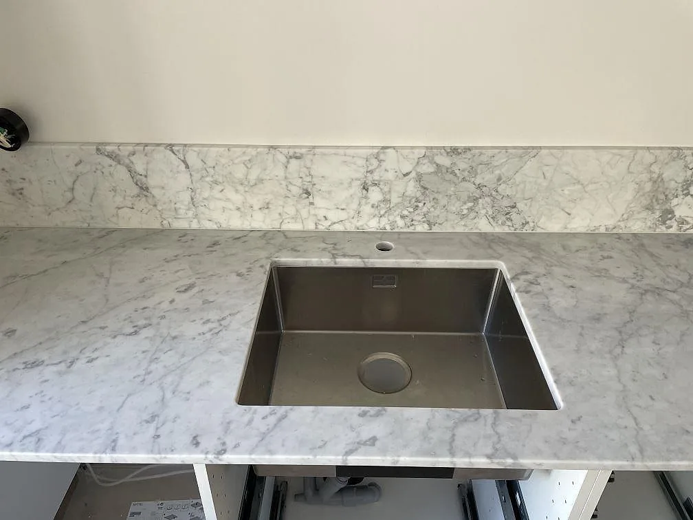 Frontvy av underlimmad rostfri diskho i en matt Carrara C-marmorbänkskiva med stänkskydd i Lindome.