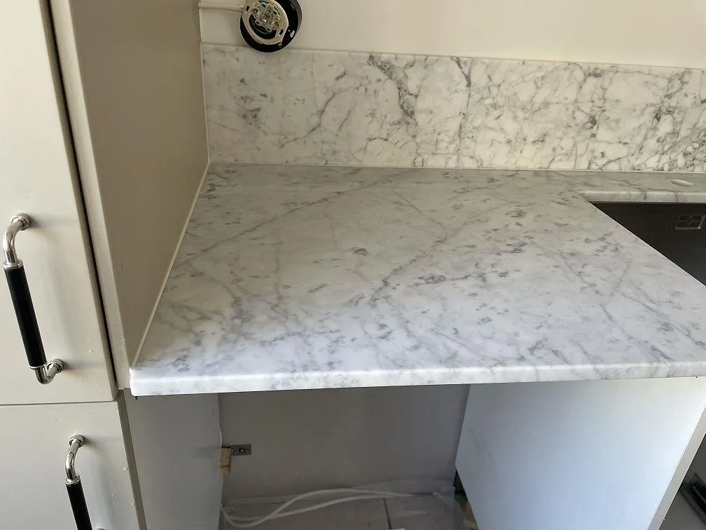 Vänster bänkdel i matt Carrara C-marmor med stänkskydd och synlig rostfri diskho vid kanten i Lindome.