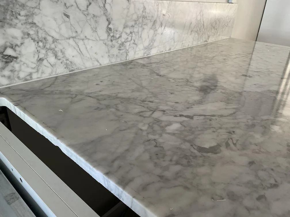 Detalj av matt Carrara C-marmorskiva och stänkskydd med grå ådring längs köksväggen i Lindome.