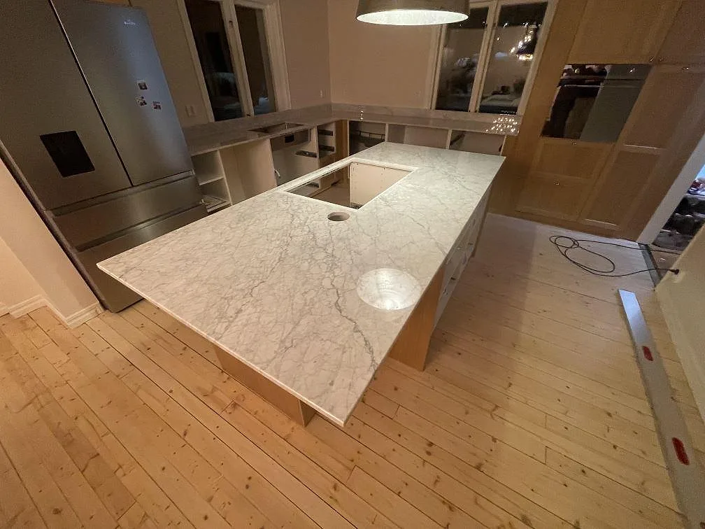 Köksö i vit Carrara C marmor med polerad yta och tydlig grå ådring i ett kök under montering i Linköping.