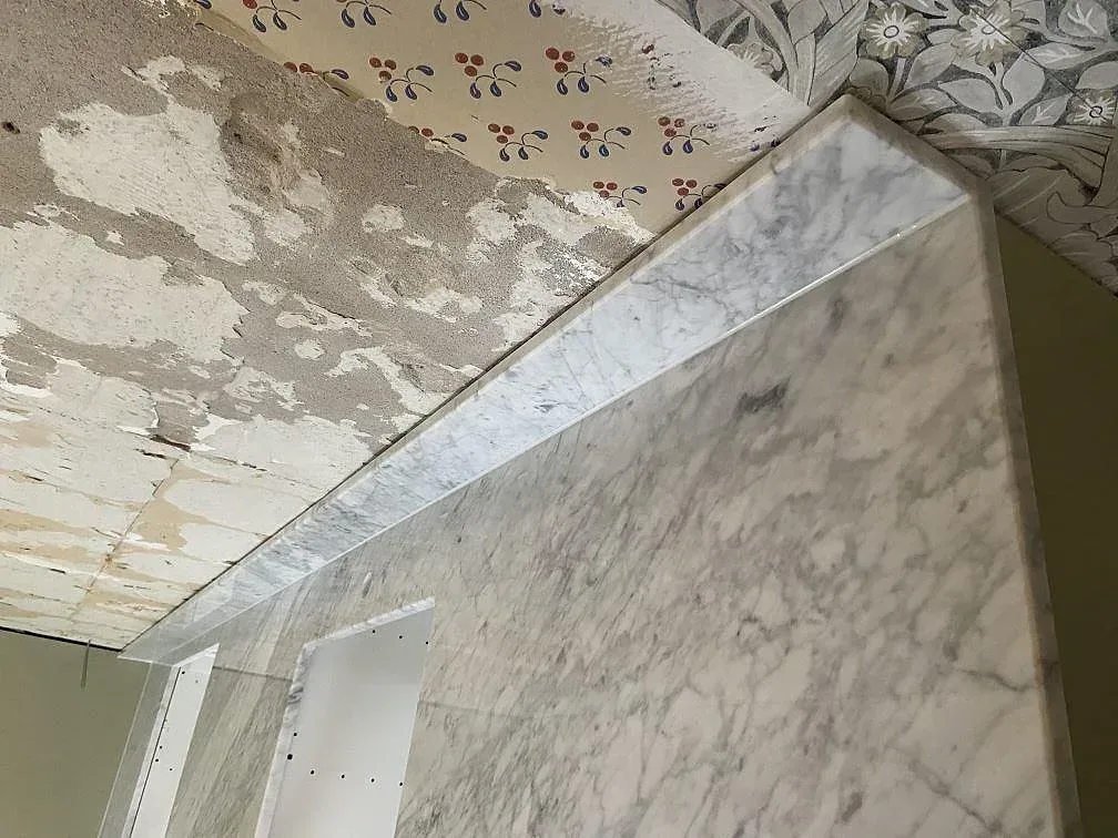 Köksbänkskiva i vit Carrara C-marmor, polerad, med uppvikt stänkkant och tydlig grå ådring i ett kök under montering i Löddeköpinge.