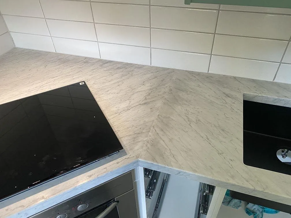 Hörnparti av köksbänkskiva i Carrara C marmor med induktionshäll och underlimmad diskho i ett kök i Löddeköpinge.