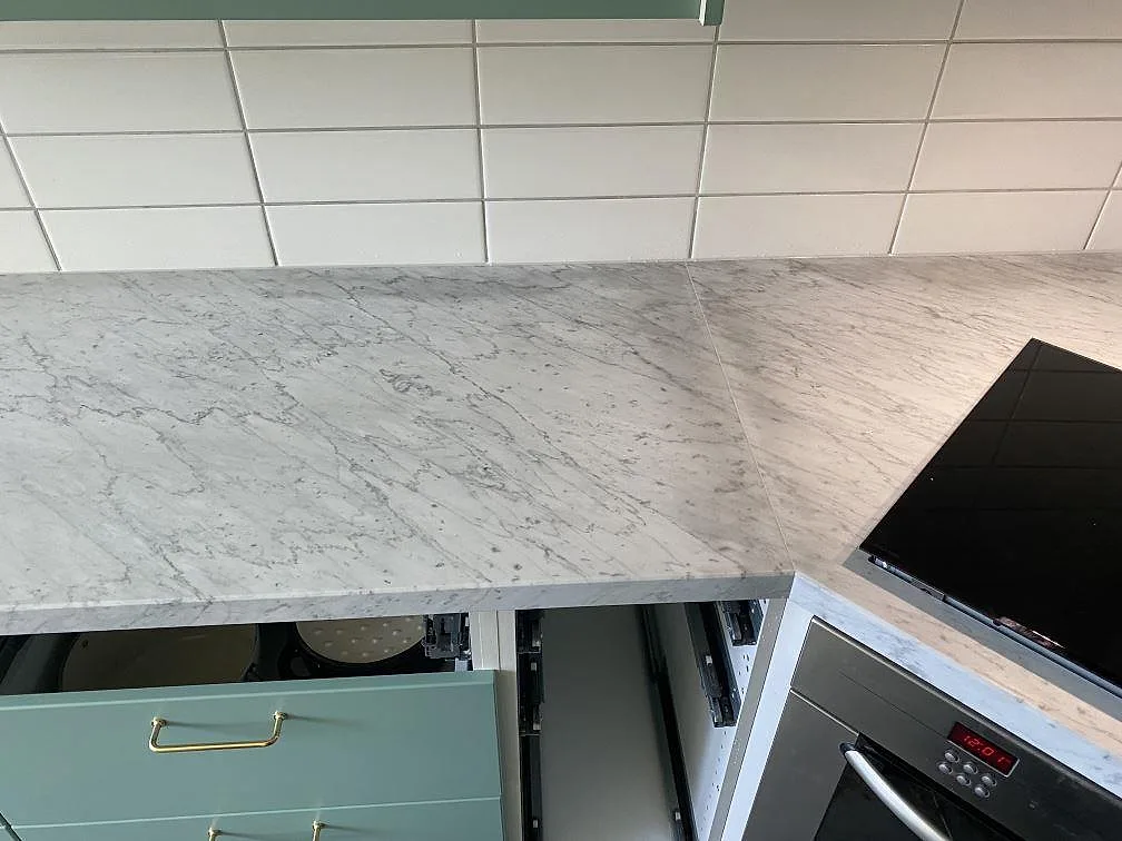 Bänkskiva i Carrara C marmor med matt yta och vit kakel som stänkskydd längs en köksrad i Löddeköpinge.