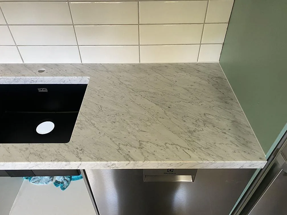 Köksbänkskiva i Carrara C marmor med underlimmad svart kompositdiskho och borrat hål för köksblandare i Löddeköpinge.