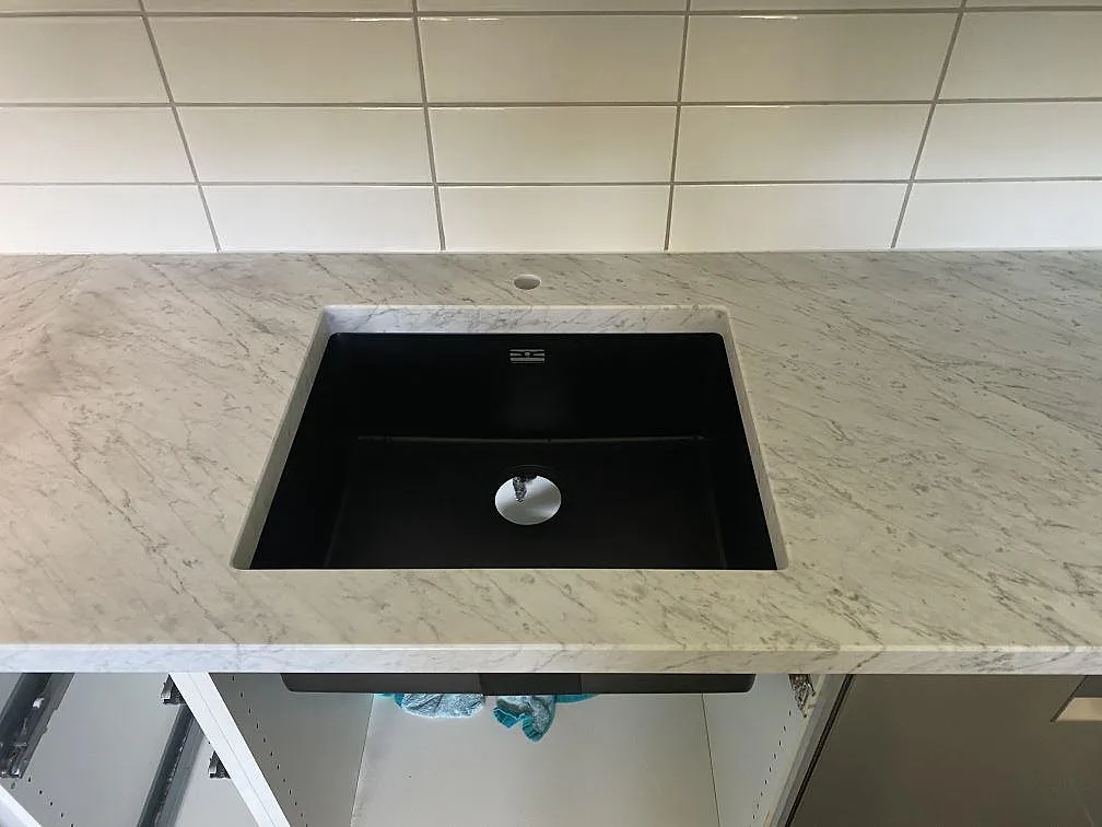 Närbild på underlimmad svart kompositdiskho i en matt köksbänkskiva av Carrara C marmor i ett kök i Löddeköpinge.