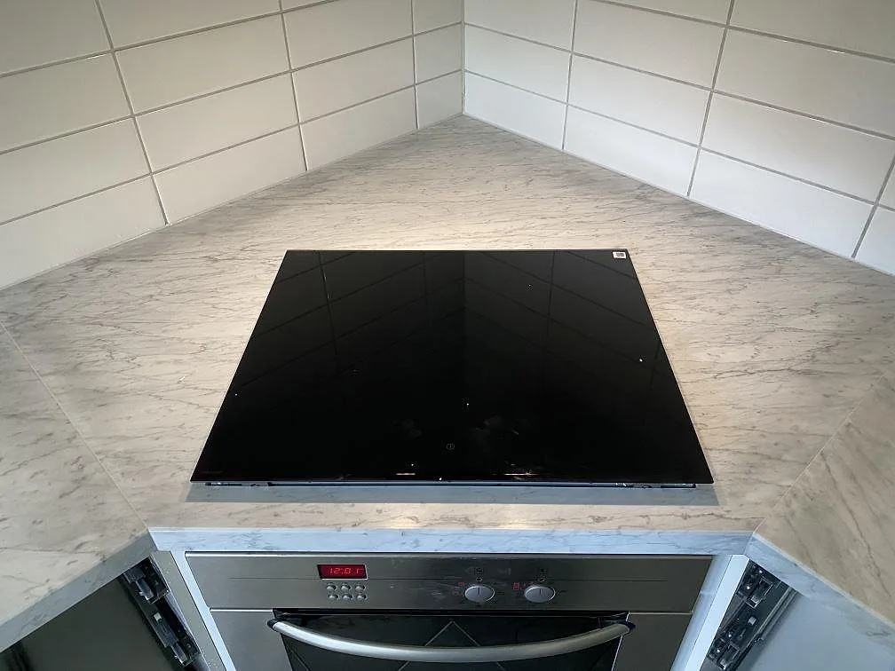 Infälld induktionshäll i en matt köksbänkskiva av Carrara C marmor med vitt kakel runt om i ett kök i Löddeköpinge.
