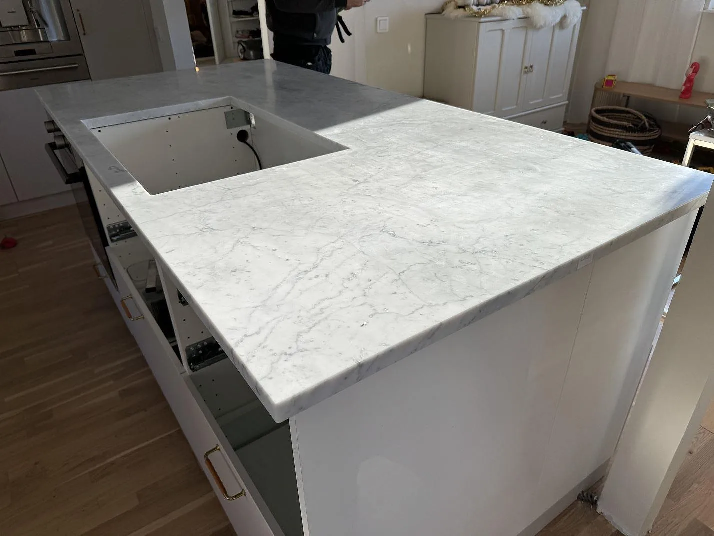 Närbild av köksö i Carrara C marmor, matt yta och tjock framkant, med hälluttag under montering i Löddeköpinge.