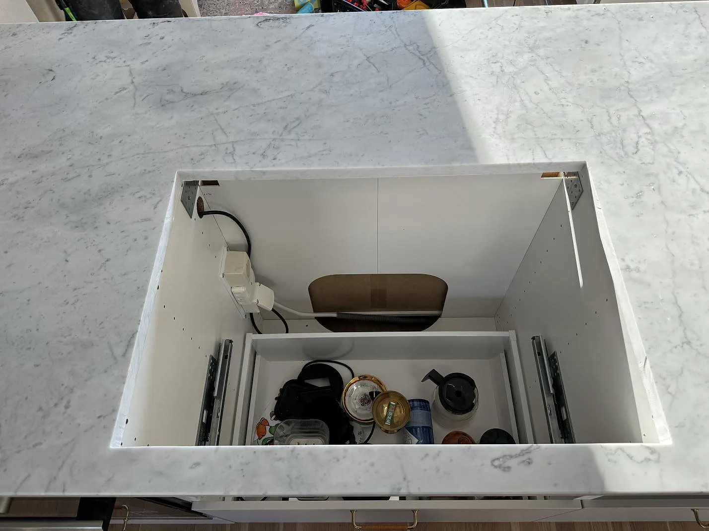 Topvy av hälluttag i en köksö av matt Carrara C marmor, monterad i vita skåpstommar i Löddeköpinge.