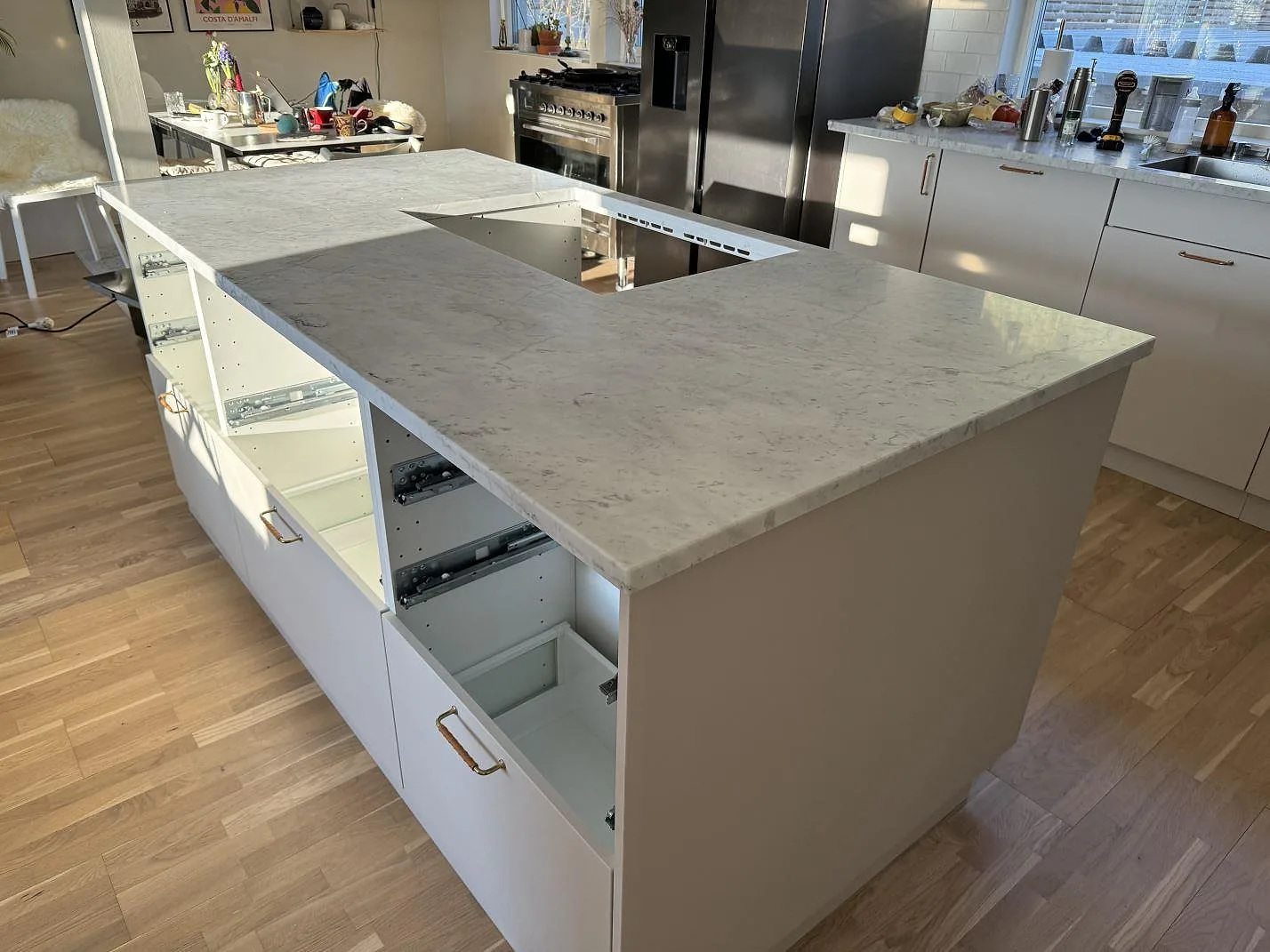 Stor köksö i Carrara C marmor, matt 30 mm, med hälluttag och vita köksskåp under montering i Löddeköpinge.