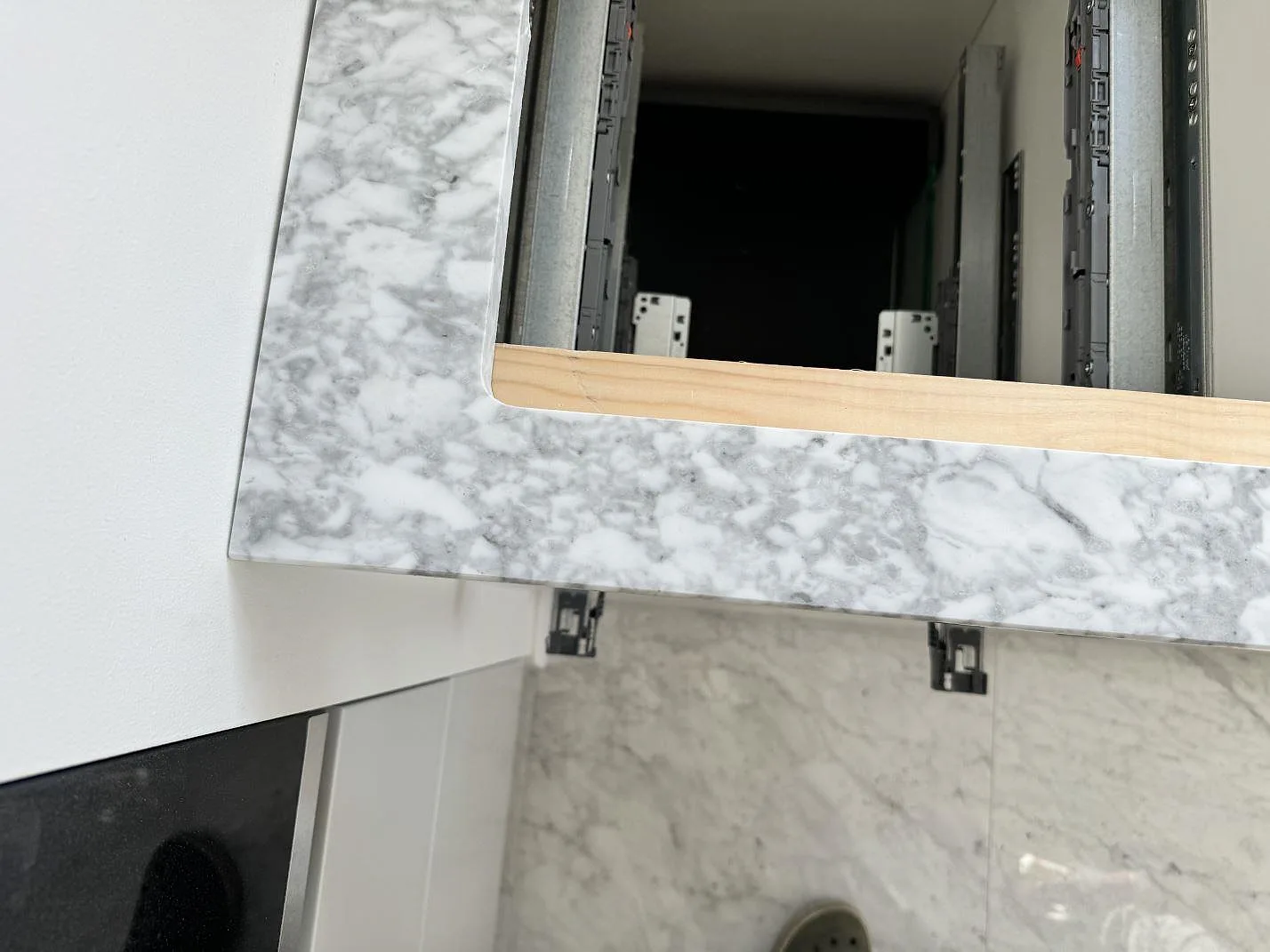 Detalj av polerad Carrara C marmor runt den öppna kommoden och vägganslutningen i Lomma.
