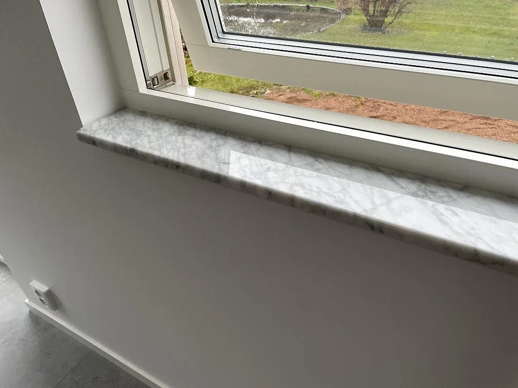 Närbild på polerad Carrara C marmor med fin grå ådring på en fönsterbänk i Lund.