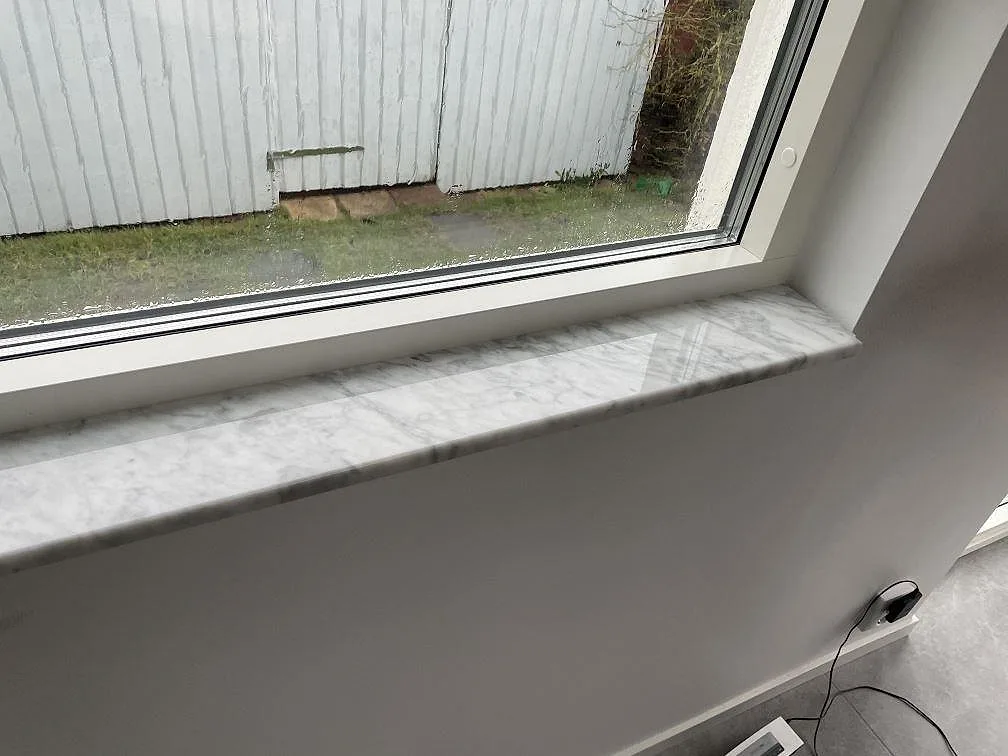 Fönsterbänk i polerad Carrara C marmor i ett ljust rum med fönster mot trädgården i Lund.
