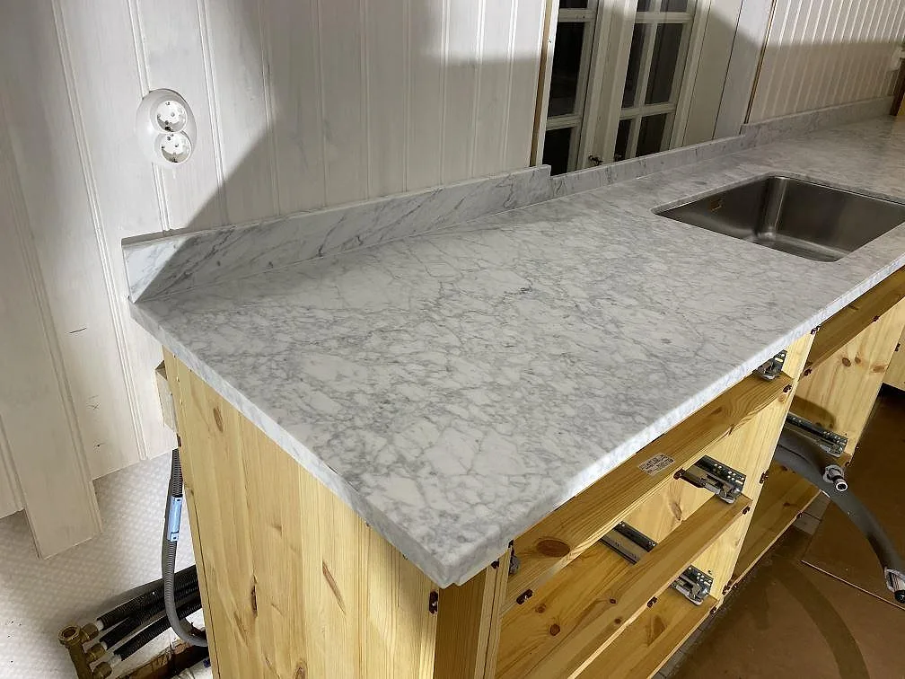 Köksbänkskiva i matt Carrara C marmor med uppvikt stänkkant och rostfri diskho i Lycke.