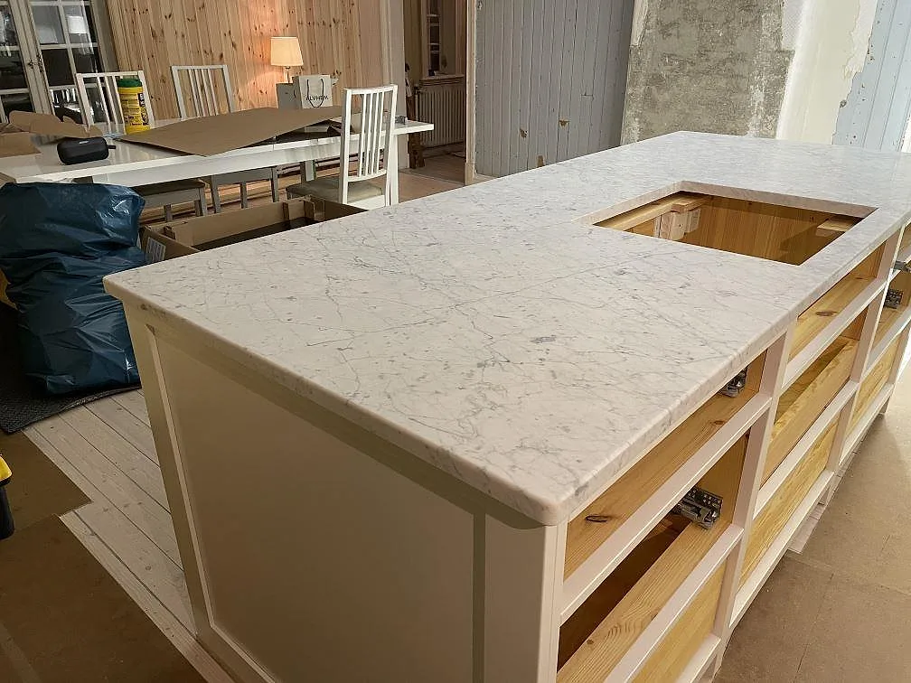 Köksö i matt Carrara C marmor med tydlig grå ådring och hällöppning under montering i Lycke.