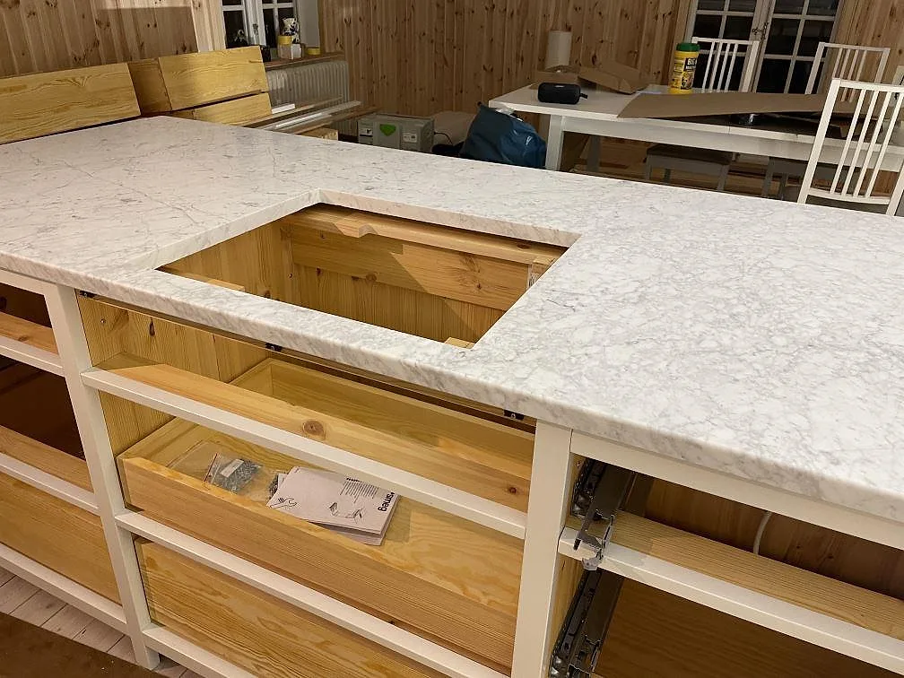 Detalj av köksö i matt Carrara C marmor med hällöppning och synliga furustommar i Lycke.