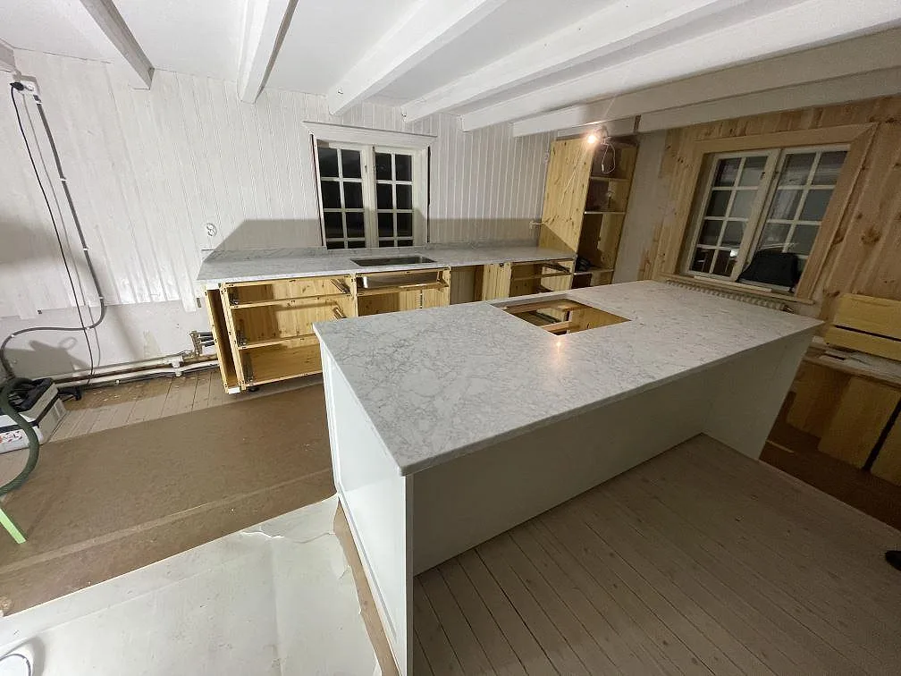 Köksbänkskiva och stor köksö i matt Carrara C marmor med hällöppning och rostfri diskho i Lycke.